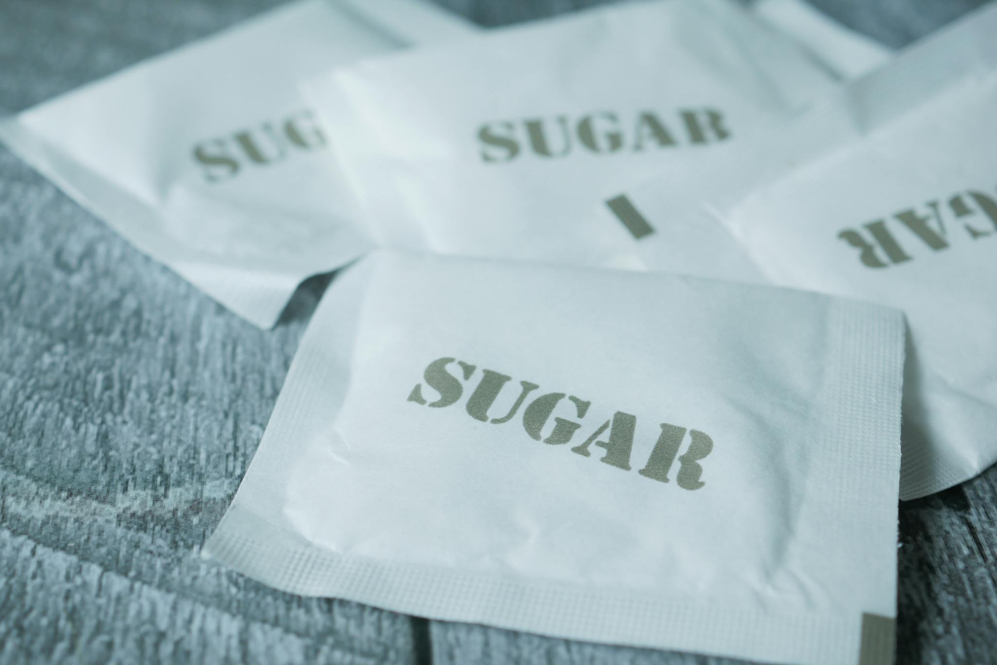 A detailed view of white sugar packets scattered on a rustic wooden surface.