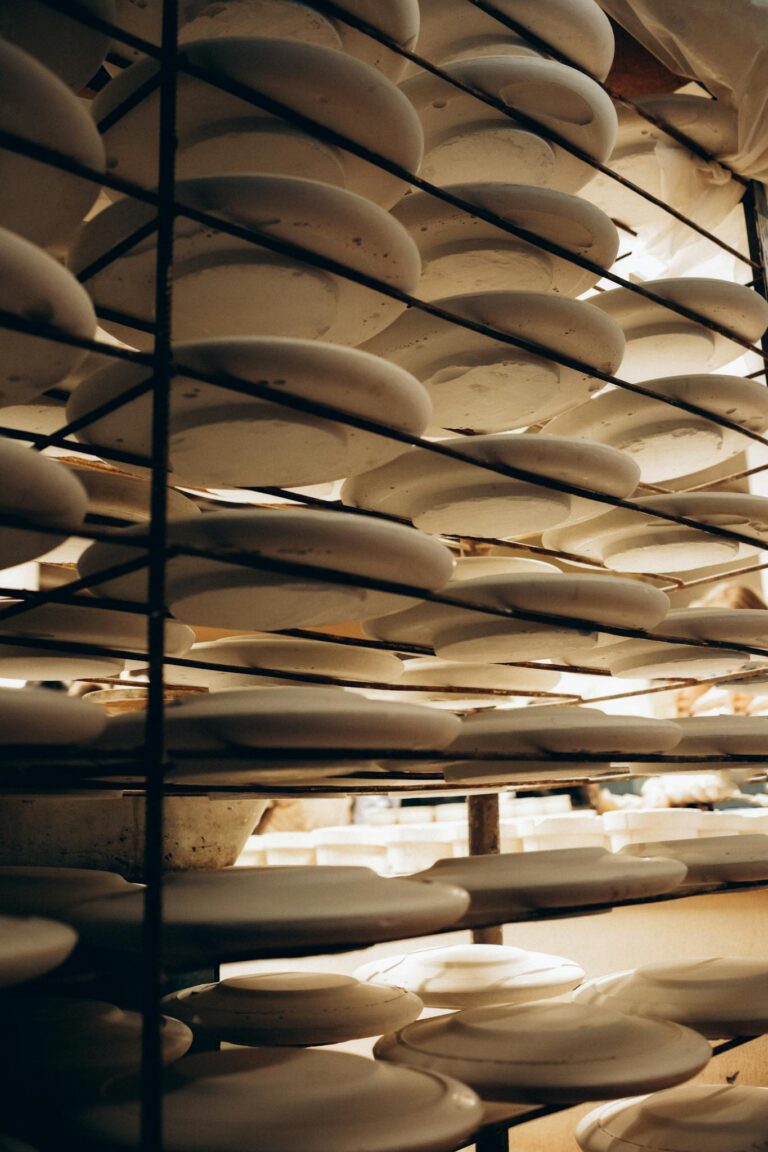 Rows of white ceramic plates stacked on metal shelves in a warm-lit kitchen setting.